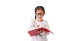 Intend little Asian child girl wearing eyeglasses holding and writes in a notebook with pencil isolated on white background with