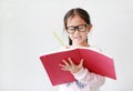 Intend little Asian girl wearing eyeglasses holding and writes in a notebook with pencil on white background