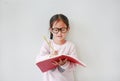 Intend little Asian girl wearing eyeglasses holding and writes in a notebook with pencil on white background