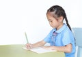 Intend little kid girl in school uniform writing on notebook at desk isolated over white background