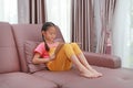 Intended Asian little young girl reading book lying on the sofa at home Royalty Free Stock Photo