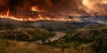 Intense wildfire blaze engulfs forest landscape with river below under dramatic sky Royalty Free Stock Photo