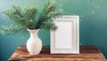 inter still life. Horizontal white frame mockup on vintage wooden bench, table. Modern white ceramic vase with pine tree branches Royalty Free Stock Photo