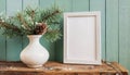 inter still life. Horizontal white frame mockup on vintage wooden bench, table. Modern white ceramic vase with pine tree branches Royalty Free Stock Photo