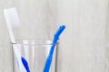 Interdental brush and toothbrush in clean glass on blurred wooden background in bathroom