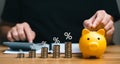 Interest rate and dividend concept. Businessman balances money in piggy bank with pile of coins and percentage symbols.