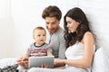 Interested baby playing on digital tablet, sitting with parents at home Royalty Free Stock Photo