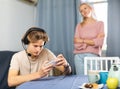 Teen boy playing game on phone against background of frustrated mother Royalty Free Stock Photo