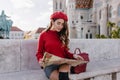 Interested female tourist in knitted sweater looking at map, resting after excursion. Elegant curly girl in red beret Royalty Free Stock Photo