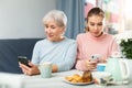Interested girl and elderly mother absorbedly staring at smartphones Royalty Free Stock Photo