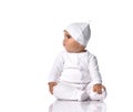 Curious infant baby toddler sits on the floor in white onepiece jumpsuit overall and funny hat with ears and looks aside