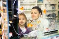 Girl with mother behind glass aquarium choosing fish Royalty Free Stock Photo