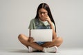 Interested student teen girl in glasses watching lection class on laptop on gray background.