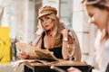 Interested young woman looking around, holding newspaper and drinking wine. Outdoor portrait of lovely girl wears cap Royalty Free Stock Photo