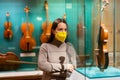 Woman in mask viewing collections of ancient musical instruments in museum
