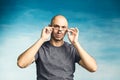 An interesting bald man adjusts his glasses with his hands and looks in surprise at the camera on a blue background Royalty Free Stock Photo