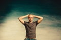 An interesting bald man in red glasses stands against a blue wall with his hands behind his head Royalty Free Stock Photo