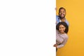 Interesting Offer. Happy Young Black Couple Peeping Out Behind White Advertisement Board Royalty Free Stock Photo