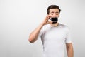 An interesting picture of a guy standing near big white wall and closing his mouth with a phone in his right hand. He Royalty Free Stock Photo