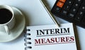 INTERIM MEASURES - words written in a notebook against the background of a calculator and a cup of coffee Royalty Free Stock Photo