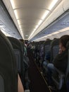 Interior of airplane with passengers sitting on seats and stewardess walking the aisle in background