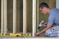 Interior of attic insulated room with oak floor under reconstruction. Young professional worker uses level and screwdriver install Royalty Free Stock Photo