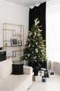 Interior of the Christmas living room with a Christmas tree and black and white gifts under it next to the sofa by the window Royalty Free Stock Photo