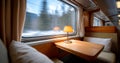 Cozy train compartment interior with wooden table, cushioned seats, and warm lamp beside window showing blurred snowy landscape Royalty Free Stock Photo