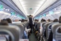 Interior of commercial airplane with stewardess serving passengers on seats during flight. Royalty Free Stock Photo