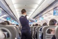 Interior of commercial airplane with stewardess serving passengers on seats during flight.