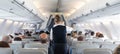 Interior of commercial airplane with stewardess serving passengers on seats during flight. Royalty Free Stock Photo