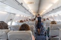 Interior of commercial airplane with stewardess serving passengers on seats during flight. Royalty Free Stock Photo