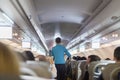 Interior of commercial airplane with stewardess serving passengers on seats during flight. Royalty Free Stock Photo