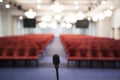 Interior of a conference room. Microphone detail of the speaker facing the room full of red chairs Royalty Free Stock Photo