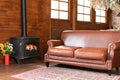 Interior cozy living room with comfortable brown leather sofa and carpet on floor. Black modern Cast iron wood stove at home. Royalty Free Stock Photo