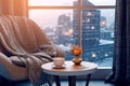 Interior with cushioned chair and table with coffee and smartphone against backdrop of winter city outside window. place