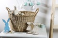 Interior decoration for Easter. rag rabbit peeks out of a wicker willow basket on the table. A garland of wooden painted eggs