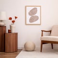 Interior design of aesthetic and elegant room with mock up poster frame, beige armchair, elegant wooden stand, glass vase with Royalty Free Stock Photo