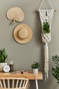 Interior design of boho living room with stylish armchair, wooden desk, house plants, cacti, rattan decoration, macrame.