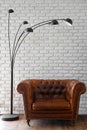 Interior design, a classic brown leather chair against a white brick wall with a modern black lamp with 5 lamps above it Royalty Free Stock Photo