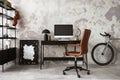 Interior design of concrete office interior with mock up poster frame, black desk, stylish brown armchair, computer screen, bike, Royalty Free Stock Photo