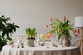 Interior design of easter dining room with colorful eggs, white hare sculptures, vase with tulips, plants, lamp, beige wall with Royalty Free Stock Photo