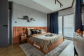 Interior design of elegant bedroom with big orange bed, beige and grey bedclothes, blue curtain, rug, modern lamp, night stand,