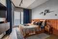 Interior design of elegant bedroom with big orange bed, beige and grey bedclothes, blue curtain, rug, modern lamp, night stand,