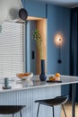 Interior design of kitchen interior with marble kitchen island, blue wall, black chokers, bowl with fruits, big window, cup,