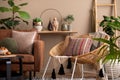 Interior design of living room interior with brown sofa, braided armchair, patterned pillows, round coffee table, stylish