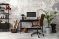 Interior design of office interior with black desk, modern dark armchair, computer screen, black lamp, simple rack, gray flower Royalty Free Stock Photo