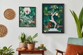 Interior design of retro living room with stylish vintage armchair, shelf, house plants, decoration and two mock up poster frames. Royalty Free Stock Photo