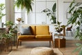 Interior design of scandinavian open space with yellow velvet sofa, plants, furniture, book, wooden cube and personal accessories