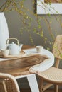 Interior design of stylish dining room interior with family wooden and epoxy table, rattan chairs, flowers in vase and teapot. Royalty Free Stock Photo